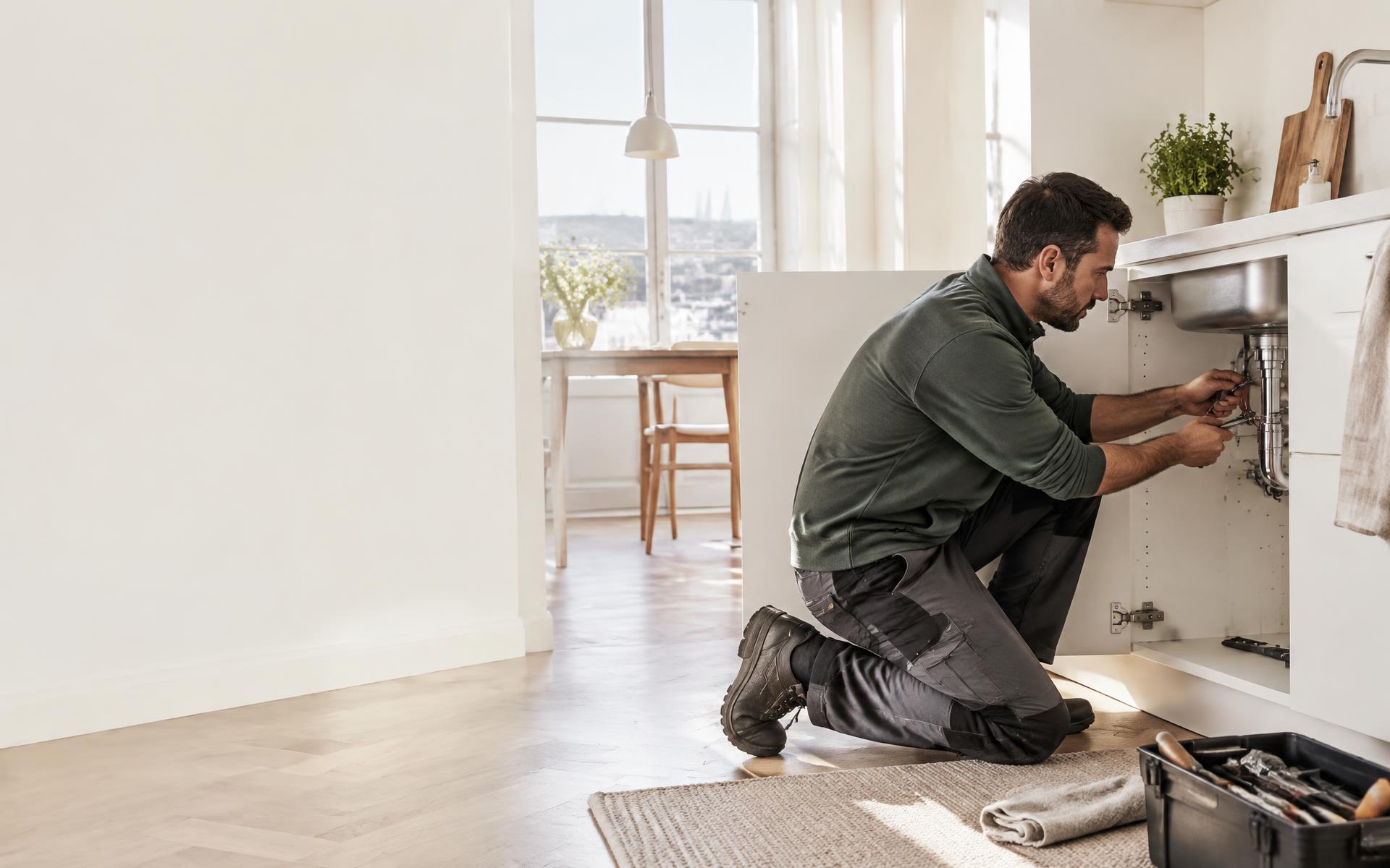 Artisan plombier au travail sous un évier dans un appartement lumineux